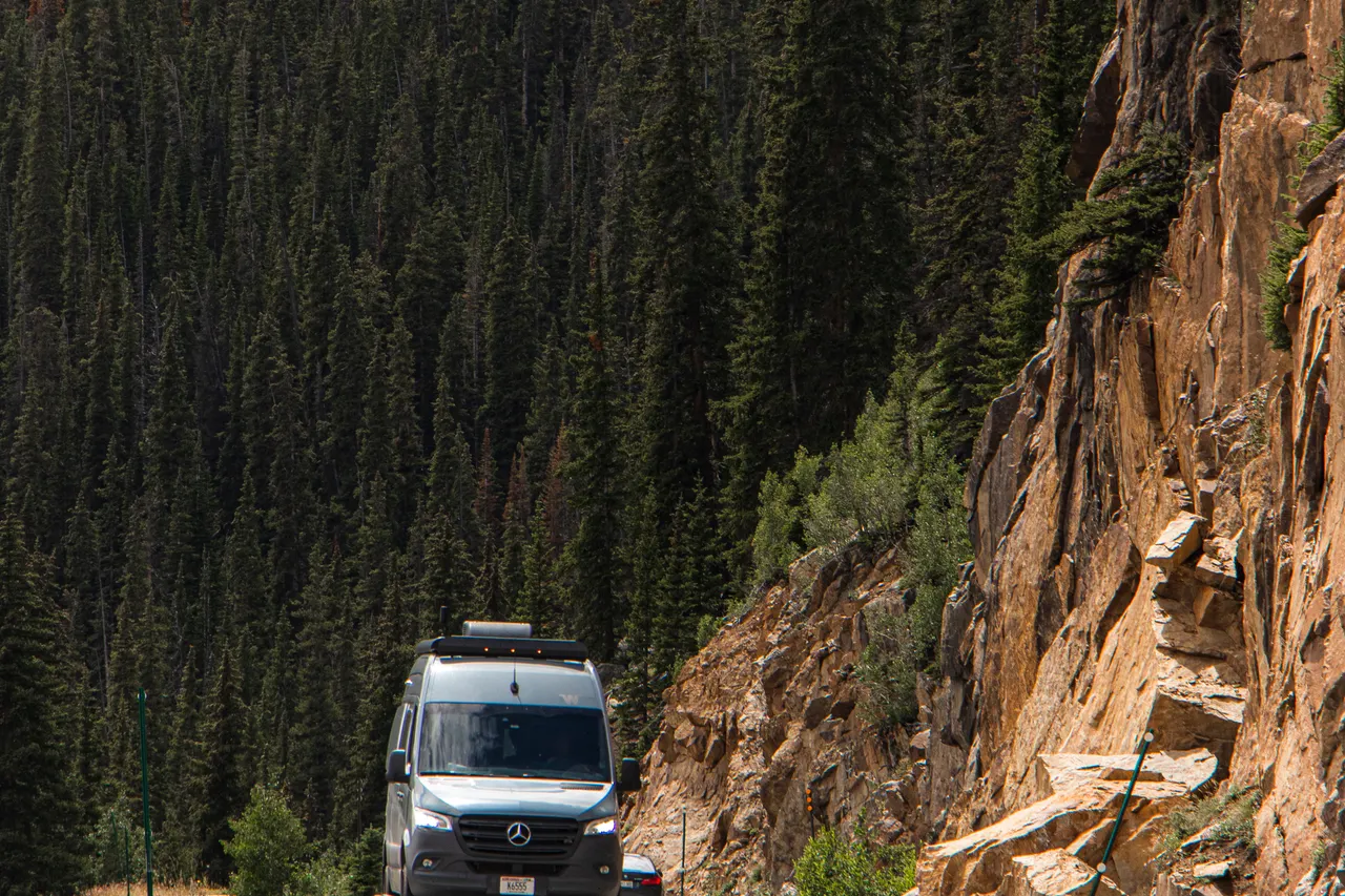 Van circulant sur une route de montagne bordée de conifères