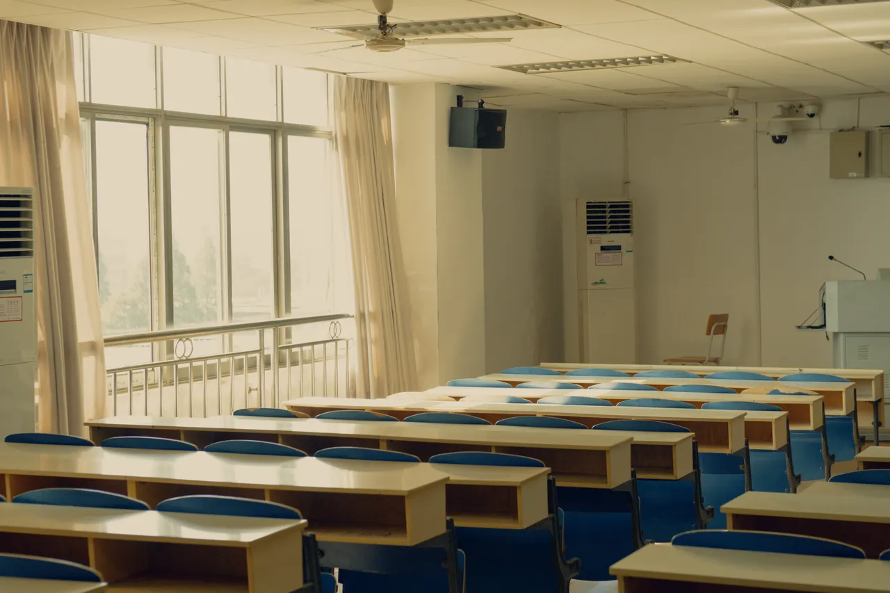 Salle de cours vide avec rangées de tables éclairées par des fenêtres